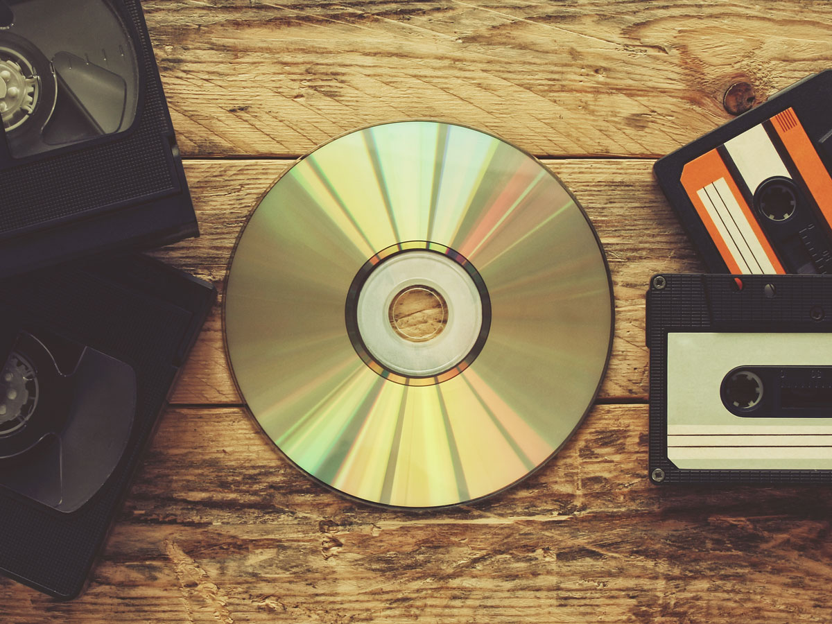Eine CD liegt auf einem Holztisch, umgeben von VHS-Kassetten und einer Audiokassette.