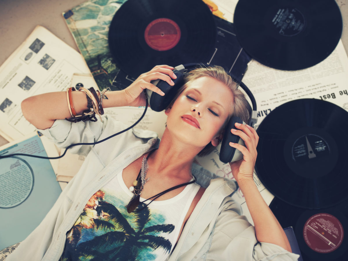 Eine Person liegt mit Kopfhörern zwischen Schallplatten und genießt Musik.