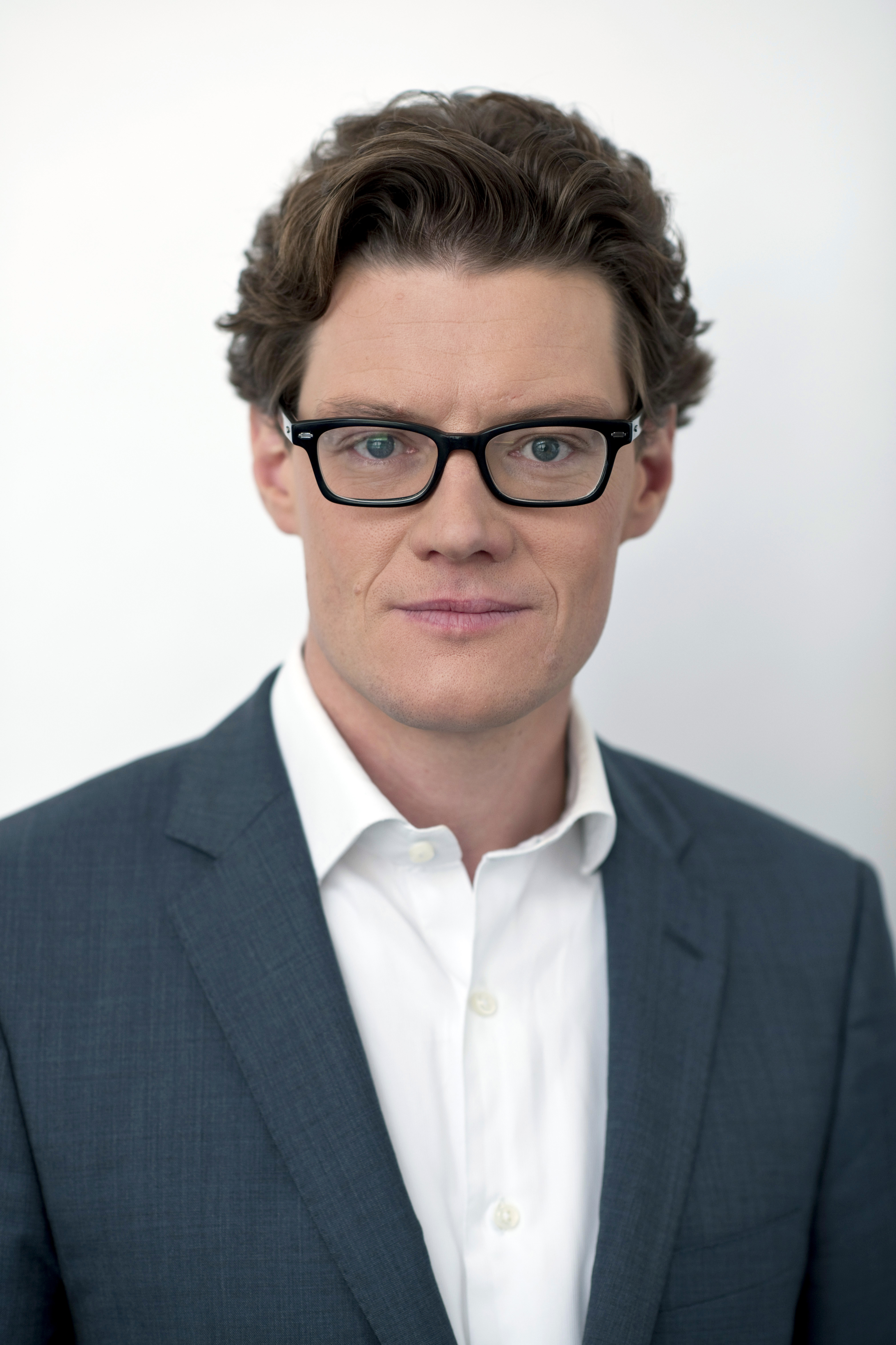 Ein Mann mit Brille im grauen Anzug vor weißem Hintergrund.