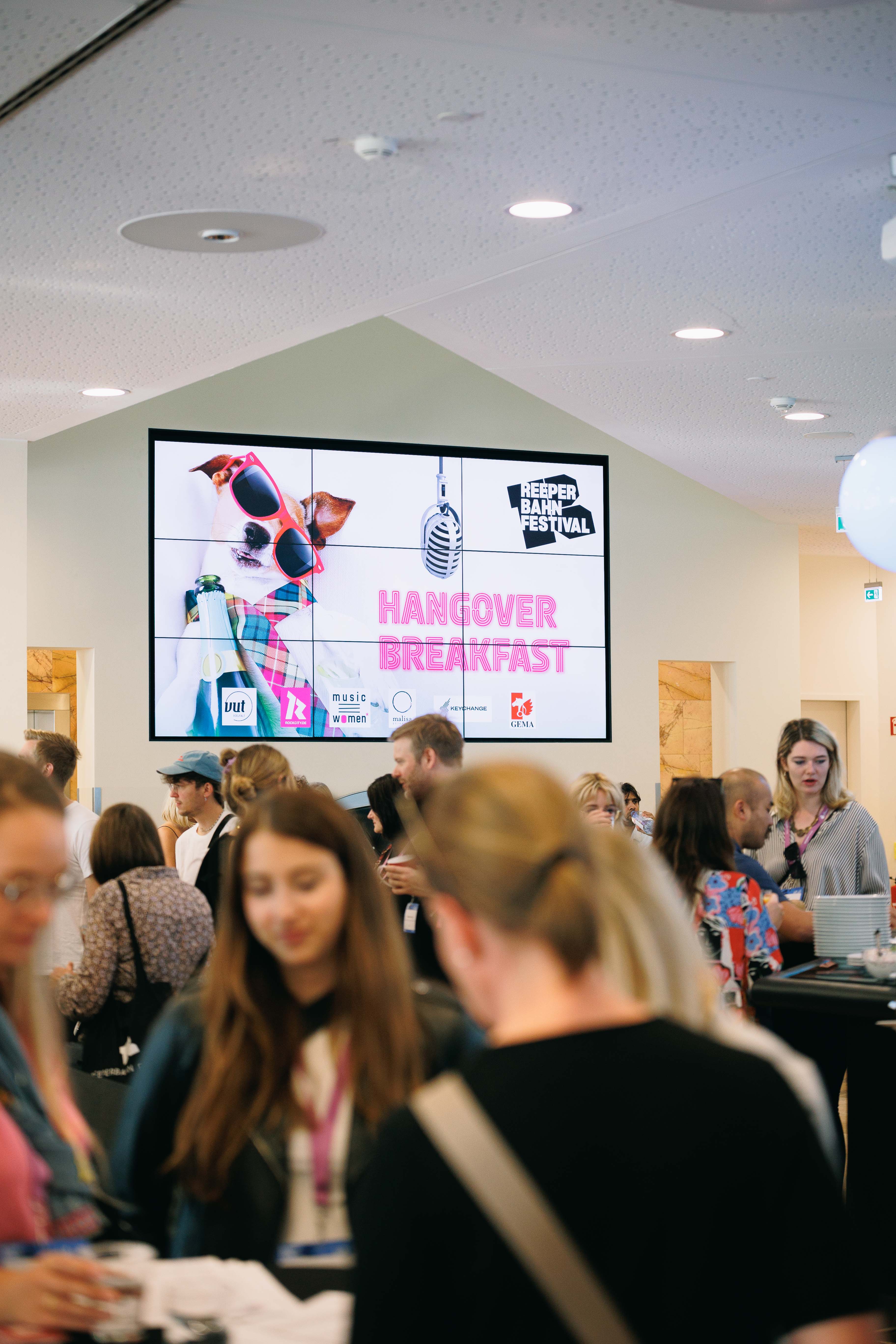 Menschenmenge vor einem Bildschirm mit Hund in Sonnenbrille, Text 