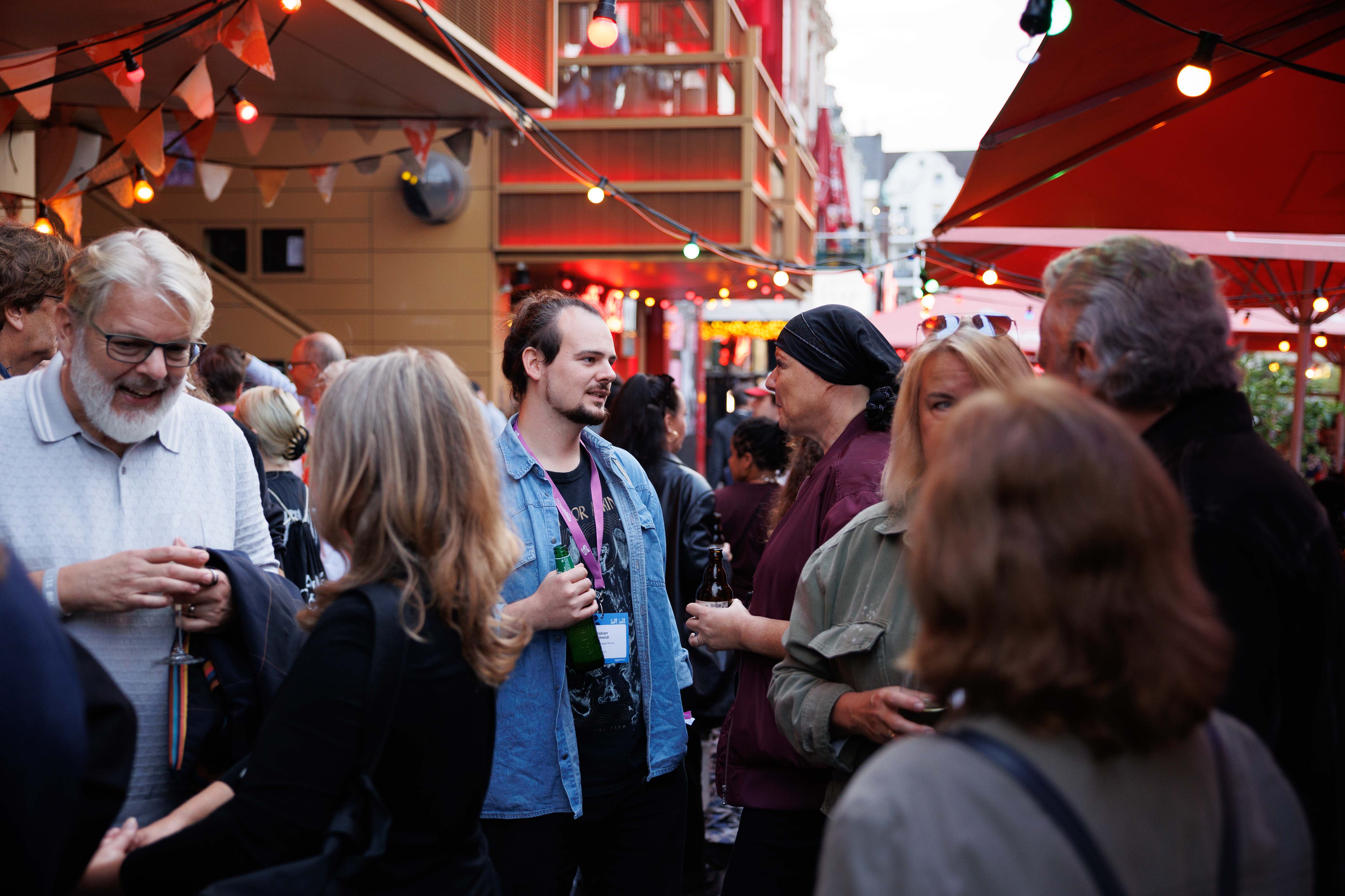 Menschen unterhalten sich bei einer Feier im Freien mit Lichterketten und roten Sonnenschirmen.
