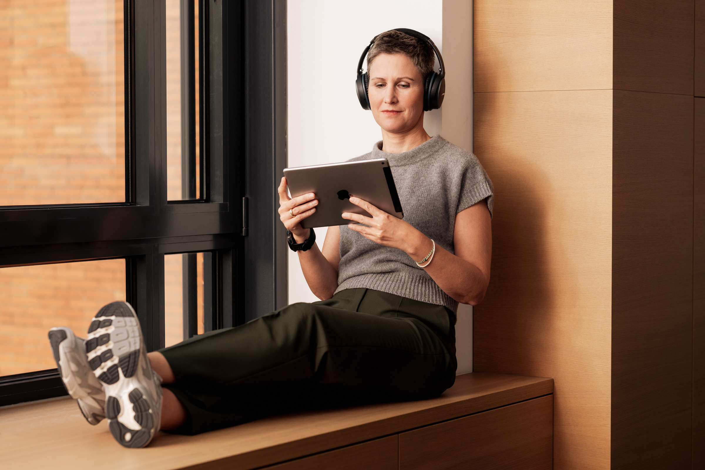 Person mit Kopfhörern sitzt am Fenster und liest auf einem Tablet.