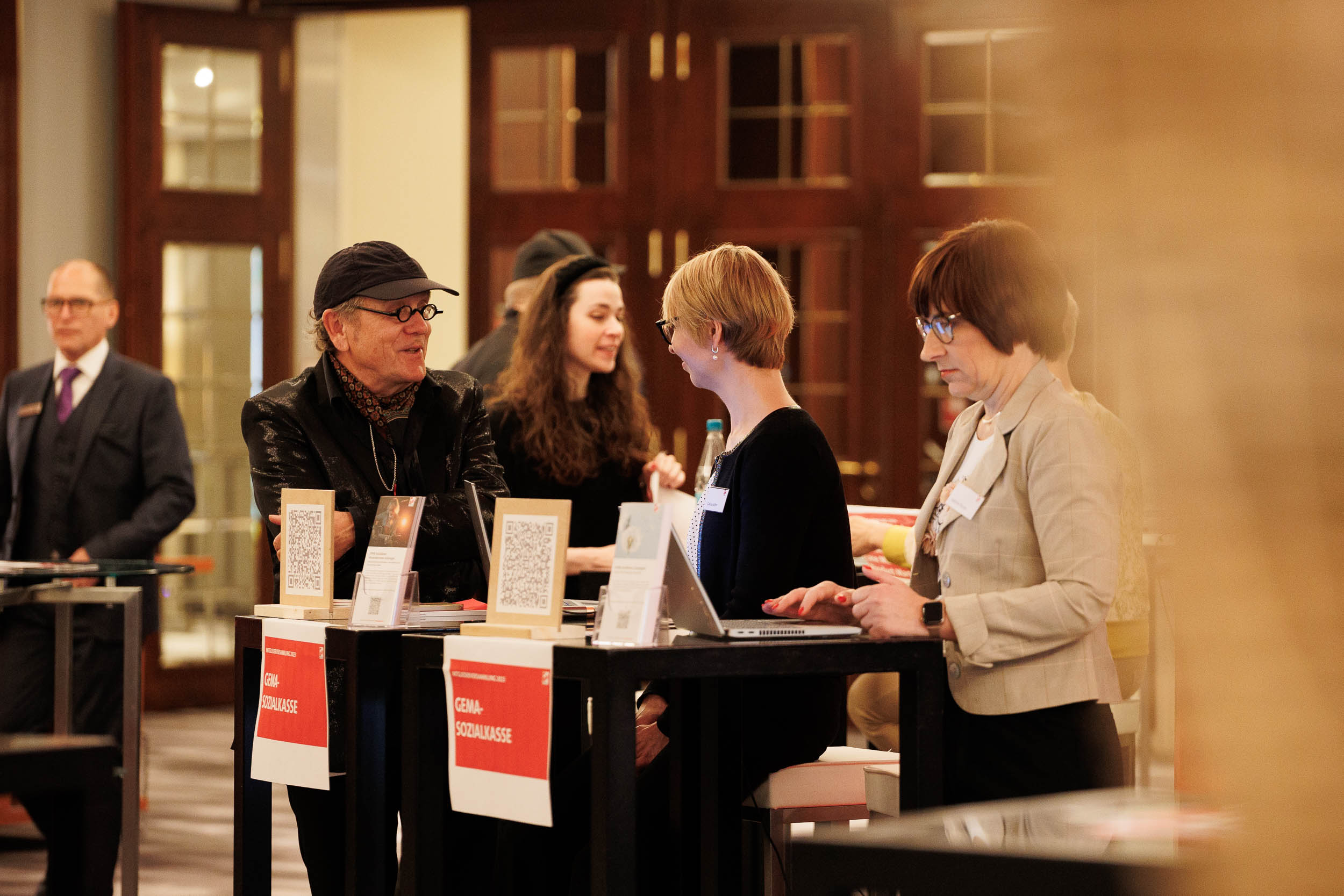 Menschen unterhalten sich an einem Infostand mit Laptops und QR-Codes in einem eleganten Raum.
