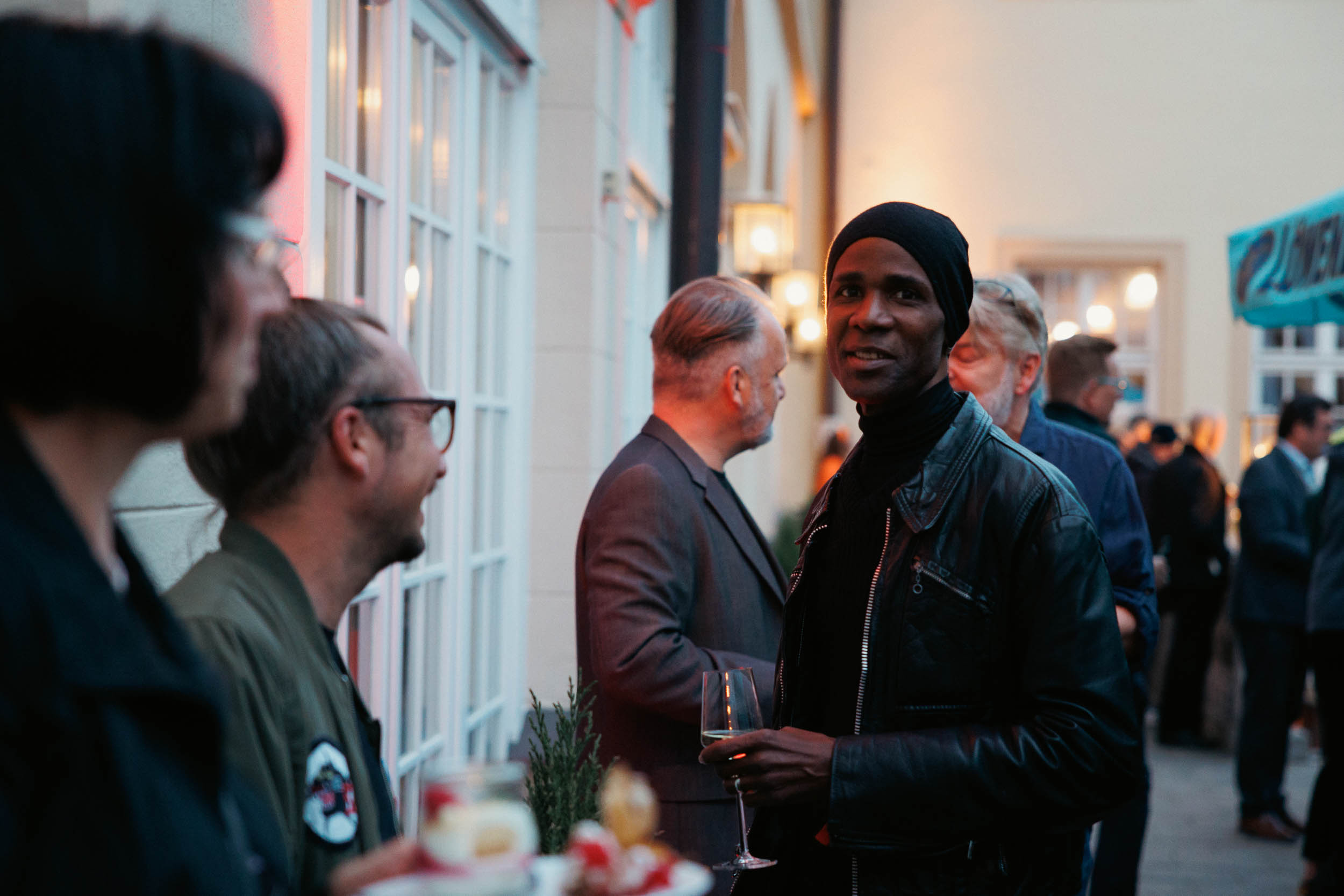 Menschen unterhalten sich bei einer Abendveranstaltung im Freien, einer hält ein Glas Wein.