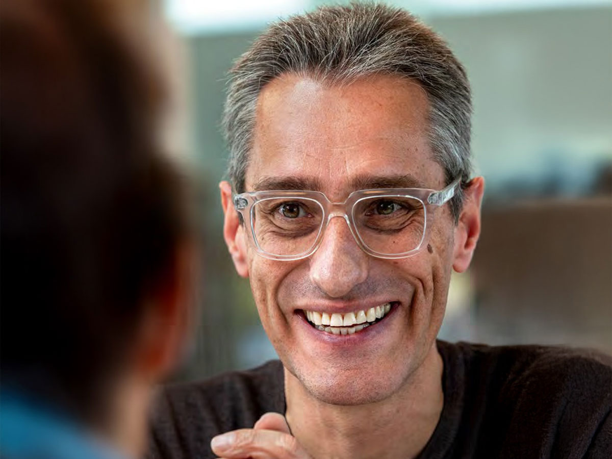 Ein Mann mit Brille lächelt und schaut eine andere Person an.