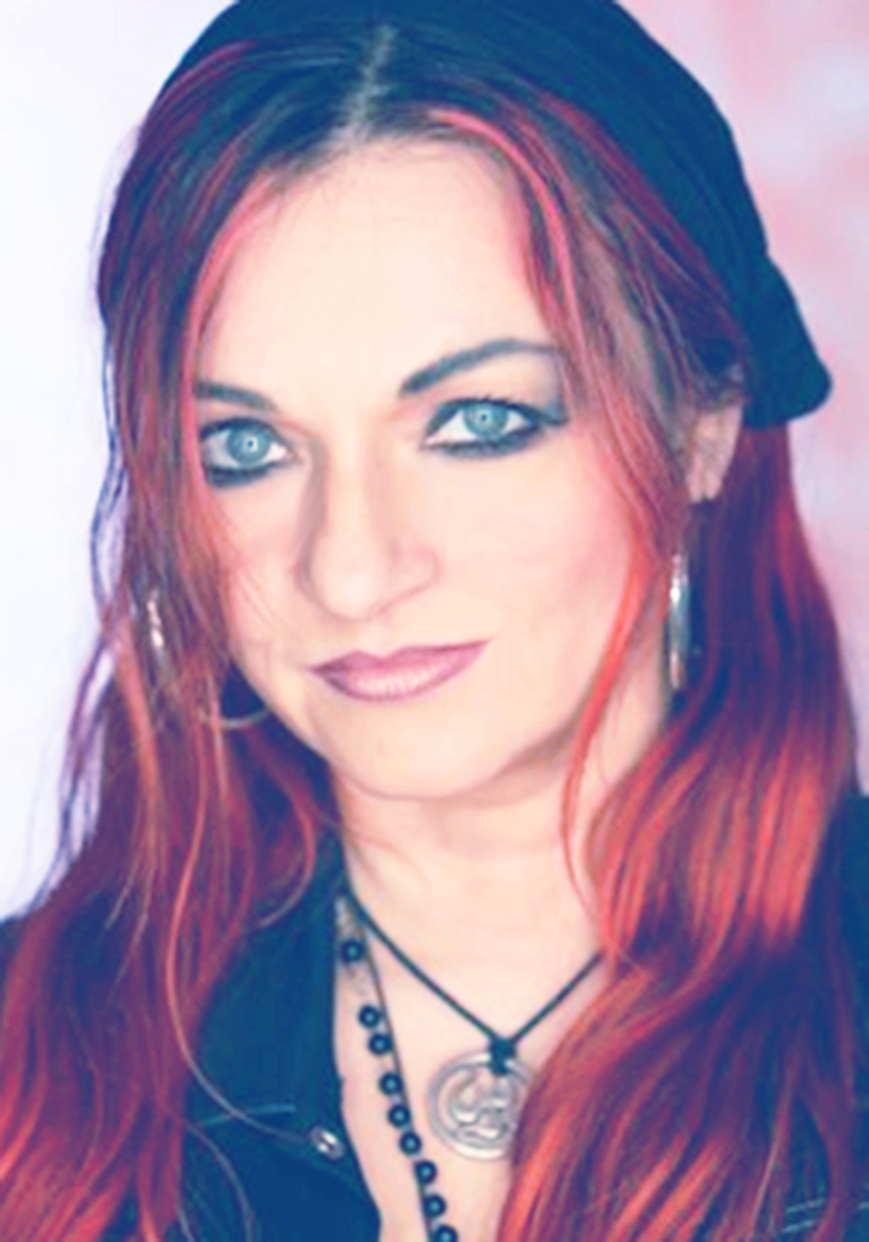 Frau mit roten Haaren und Kopftuch, trägt Ohrringe und Halskette, blickt direkt in die Kamera.