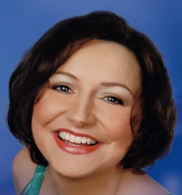 Eine lächelnde Frau mit braunen Haaren vor blauem Hintergrund.