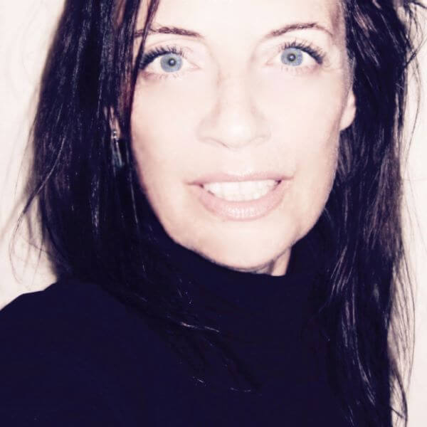 Eine Frau mit langen dunklen Haaren und blauen Augen lächelt in die Kamera.