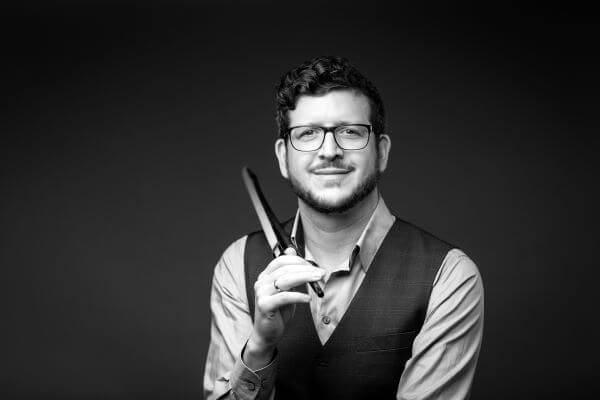 Ein Mann mit Brille hält ein Messer und lächelt in die Kamera, in Schwarz-Weiß.