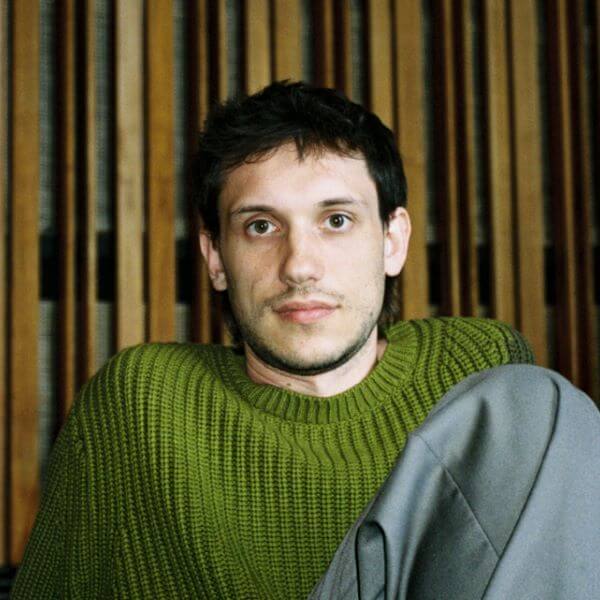 Eine Person in grünem Pullover sitzt vor einer Holzwand.