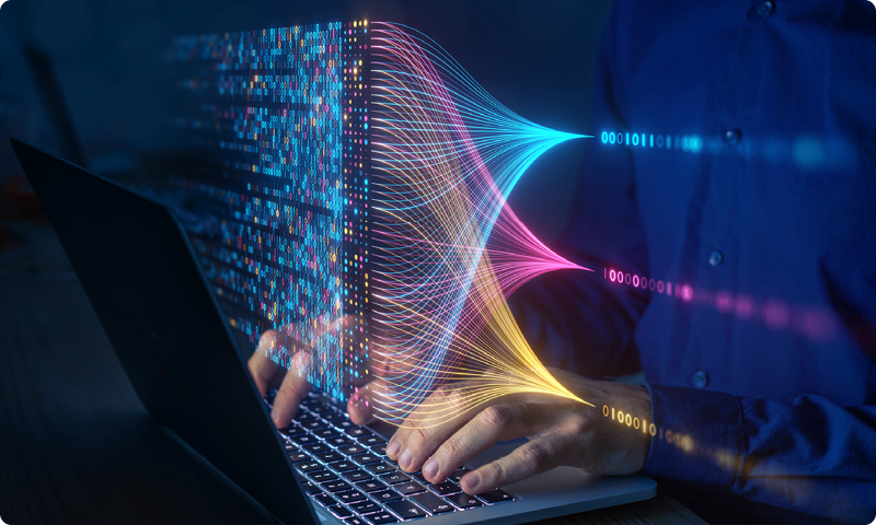Eine Person tippt auf einem Laptop, während bunte Datenströme vom Bildschirm projiziert werden.