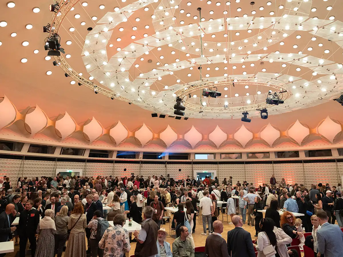 Großer, gut besuchter Veranstaltungssaal mit moderner Decke und vielen Menschen, die sich unterhalten.