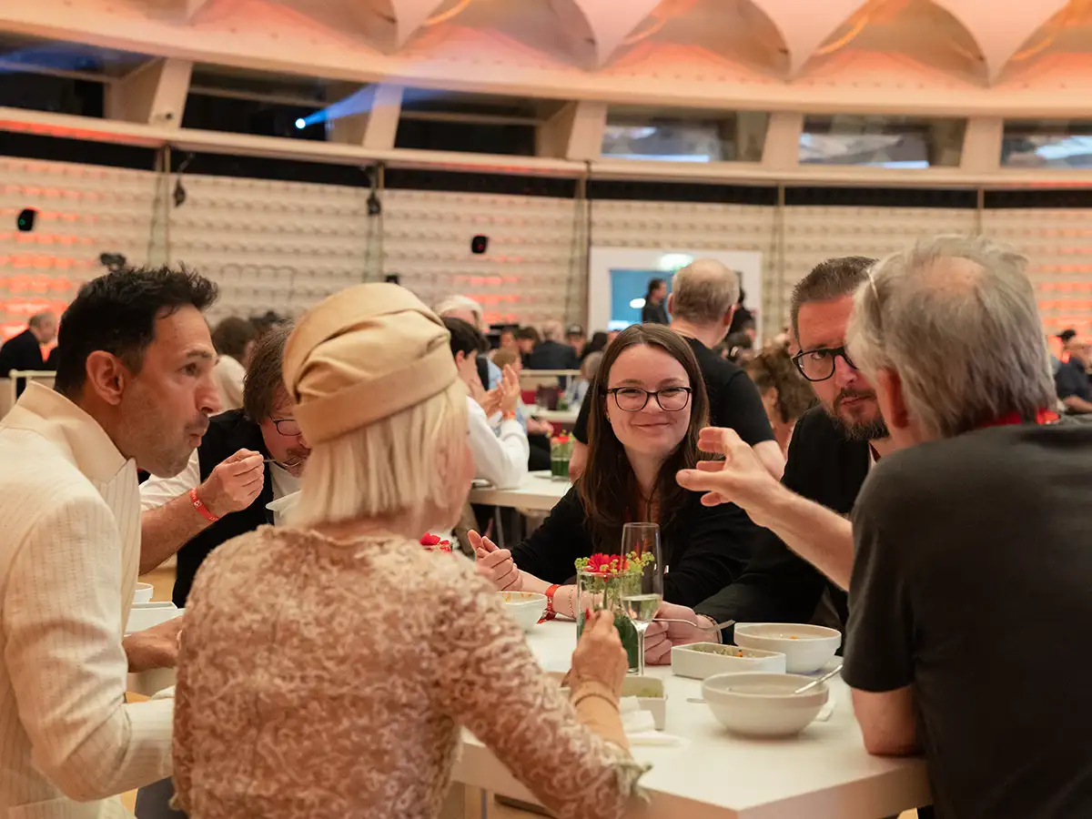 Eine Gruppe von Menschen sitzt an einem Tisch in einem eleganten Raum und unterhält sich lebhaft.