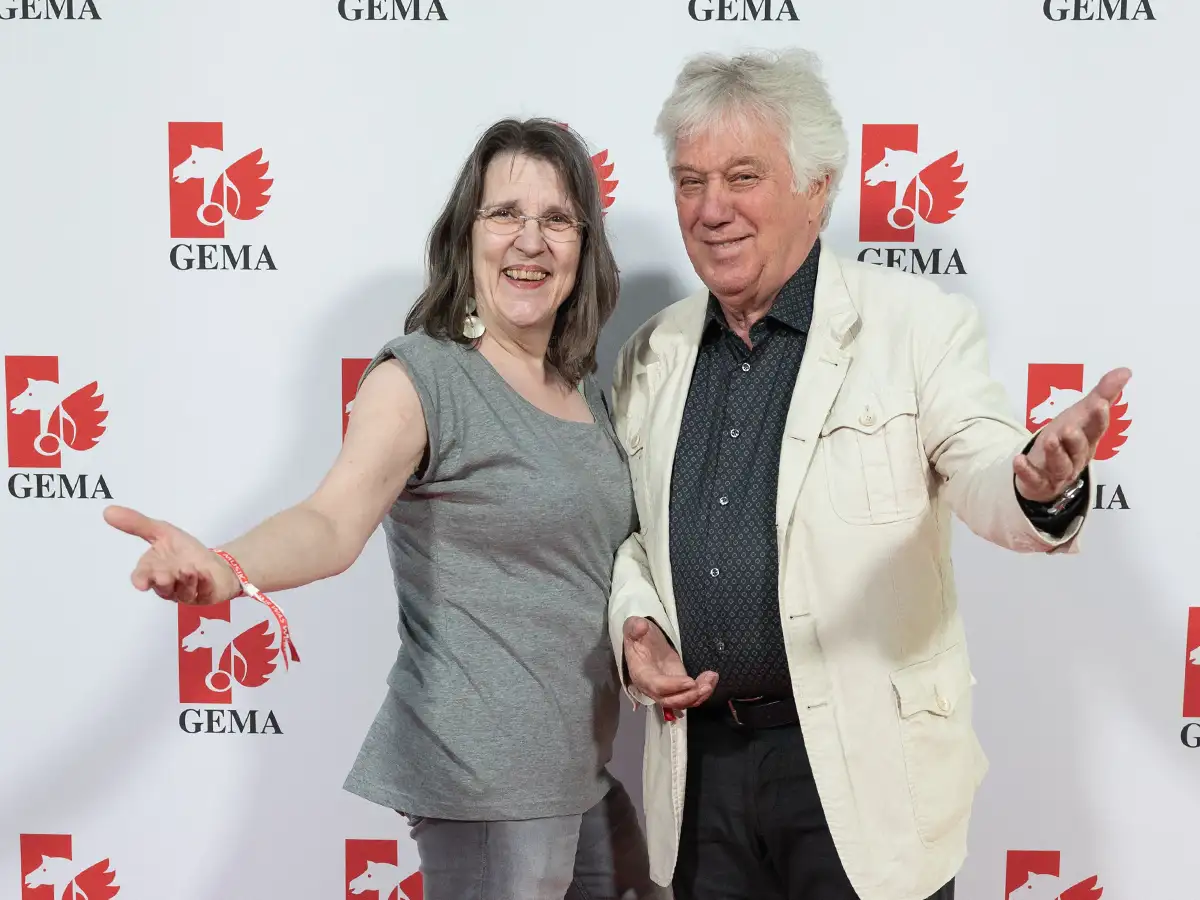 Zwei Personen lächeln und gestikulieren vor einer GEMA-Wand.