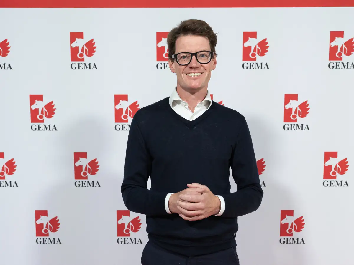 Eine Person in dunklem Pullover steht vor einer Wand mit GEMA-Logos.