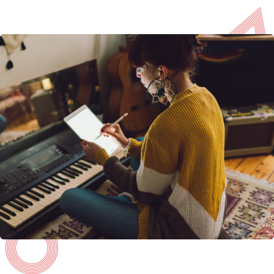 Person in gelbem Pullover schreibt mit Stift auf Tablet, sitzt neben einem Keyboard.