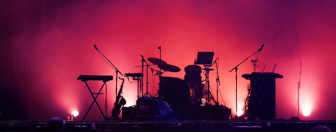 Bühne mit Schlagzeug, Keyboards und Mikrofonen vor rosa beleuchtetem Hintergrund.