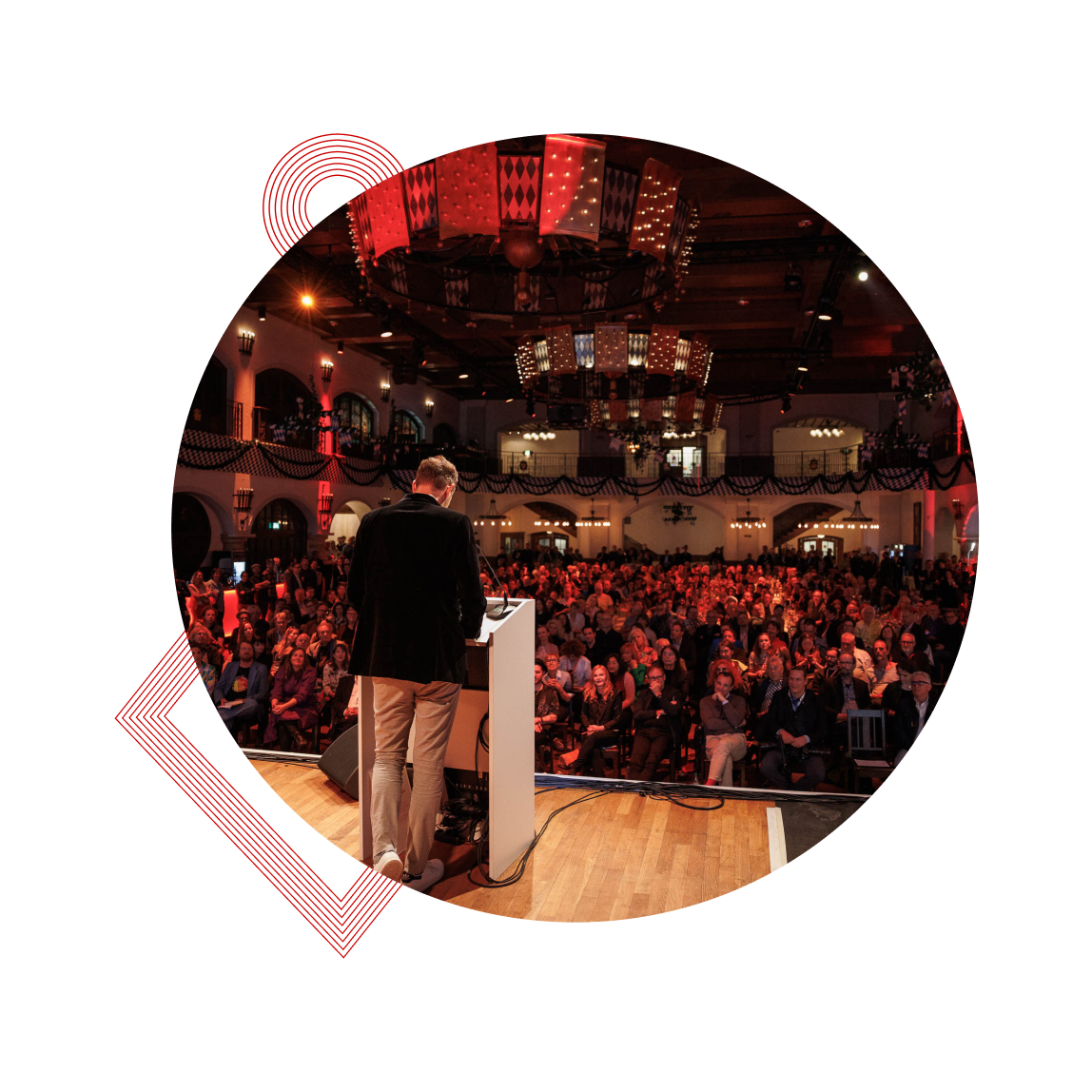 Ein Redner vor einem großen Publikum in einem festlich beleuchteten Saal.