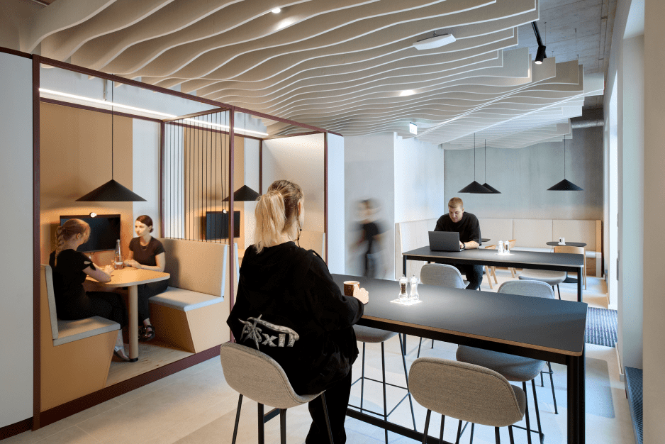 Moderne Cafeteria mit Wellen-Decke, Menschen arbeiten an Tischen, zwei Personen in einer Nische, minimalistische Lampen.