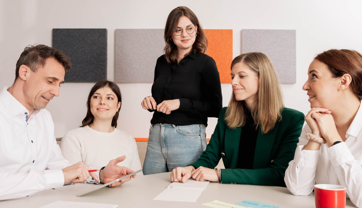 Eine Gruppe von fünf Menschen diskutiert lächelnd an einem Tisch mit Notizen.