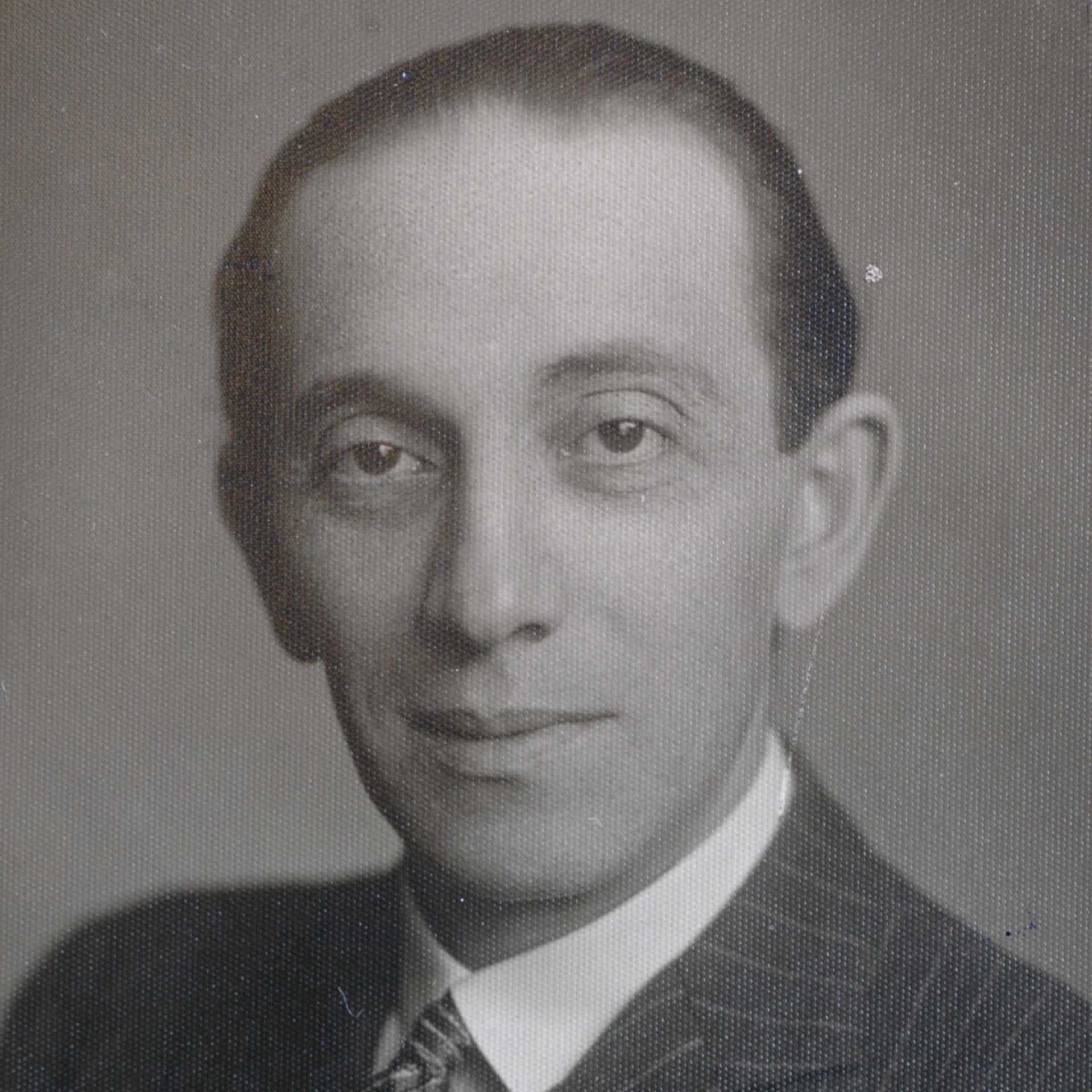 Schwarz-weiß Porträt eines Mannes im Anzug mit Krawatte, neutraler Gesichtsausdruck.