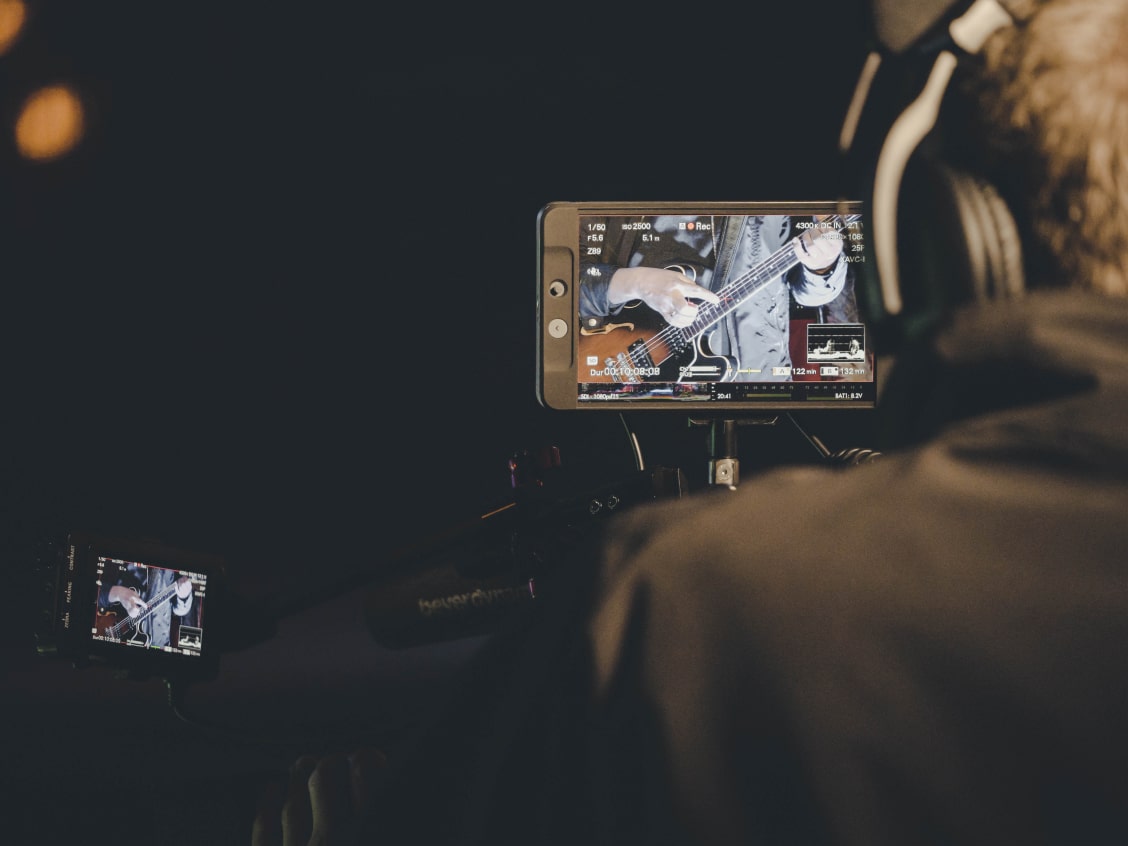 Ein Kameramann filmt einen Gitarristen, der auf dem Monitor zu sehen ist.