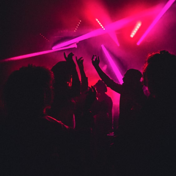 Menschen tanzen in einem Club mit pinkem Licht und Nebel.