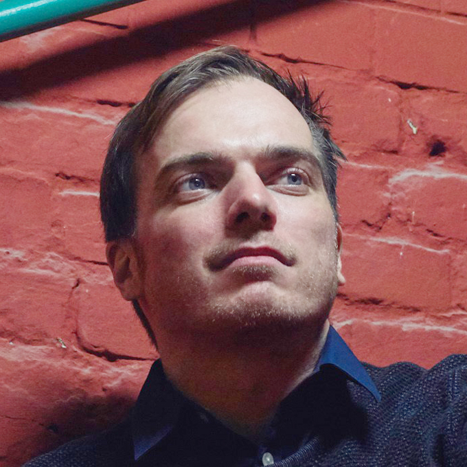 Ein Mann schaut nachdenklich vor einer roten Backsteinmauer nach oben.