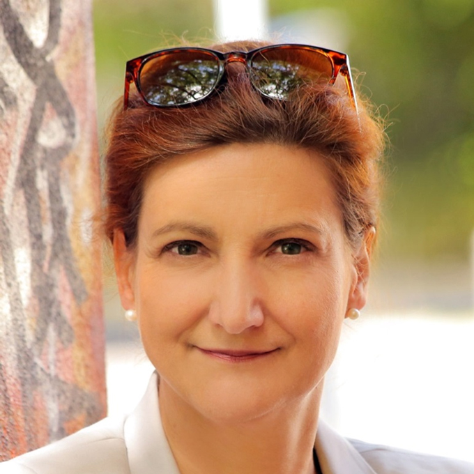 Frau mit Sonnenbrille auf dem Kopf, lächelnd, steht in der Nähe einer mit Graffiti bedeckten Wand mit unscharfem grünen Hintergrund.