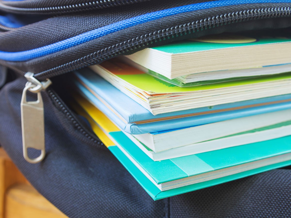 Bunte Bücher ragen aus einer offenen, schwarzen Tasche mit blauem Reißverschluss.