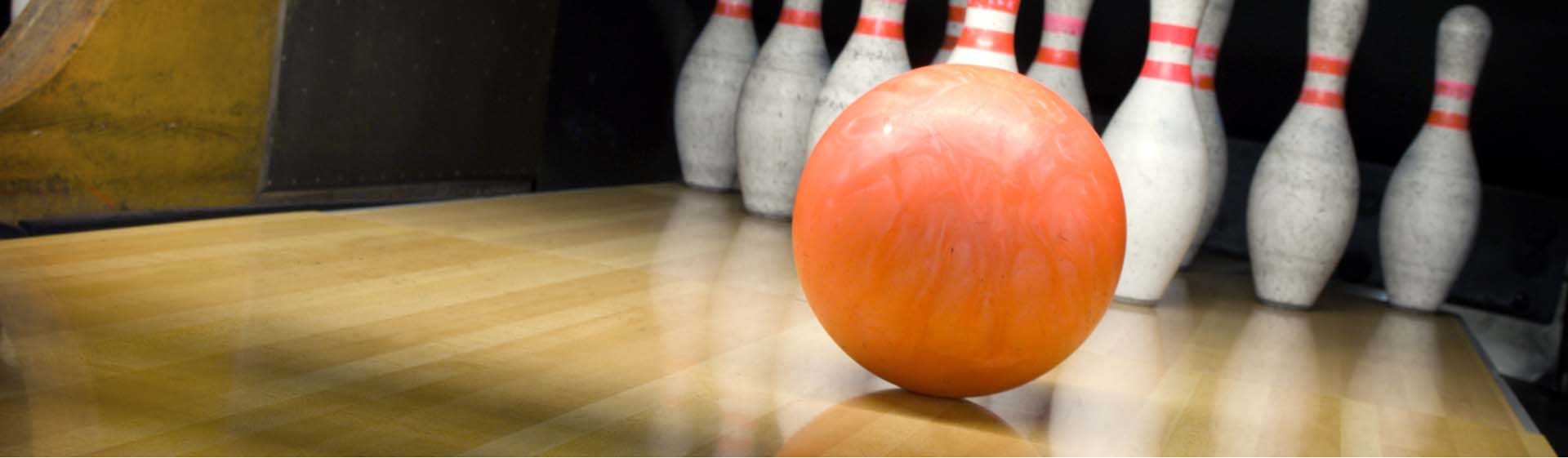 Eine orangefarbene Bowlingkugel rollt auf eine Gruppe von Kegeln zu.