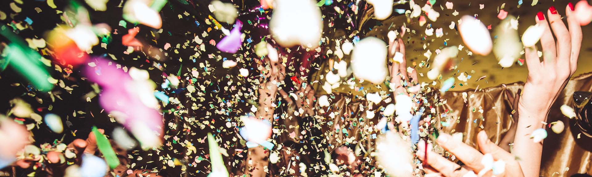 Bunte Konfetti fliegen durch die Luft, umgeben von jubelnden Händen mit rotem Nagellack.