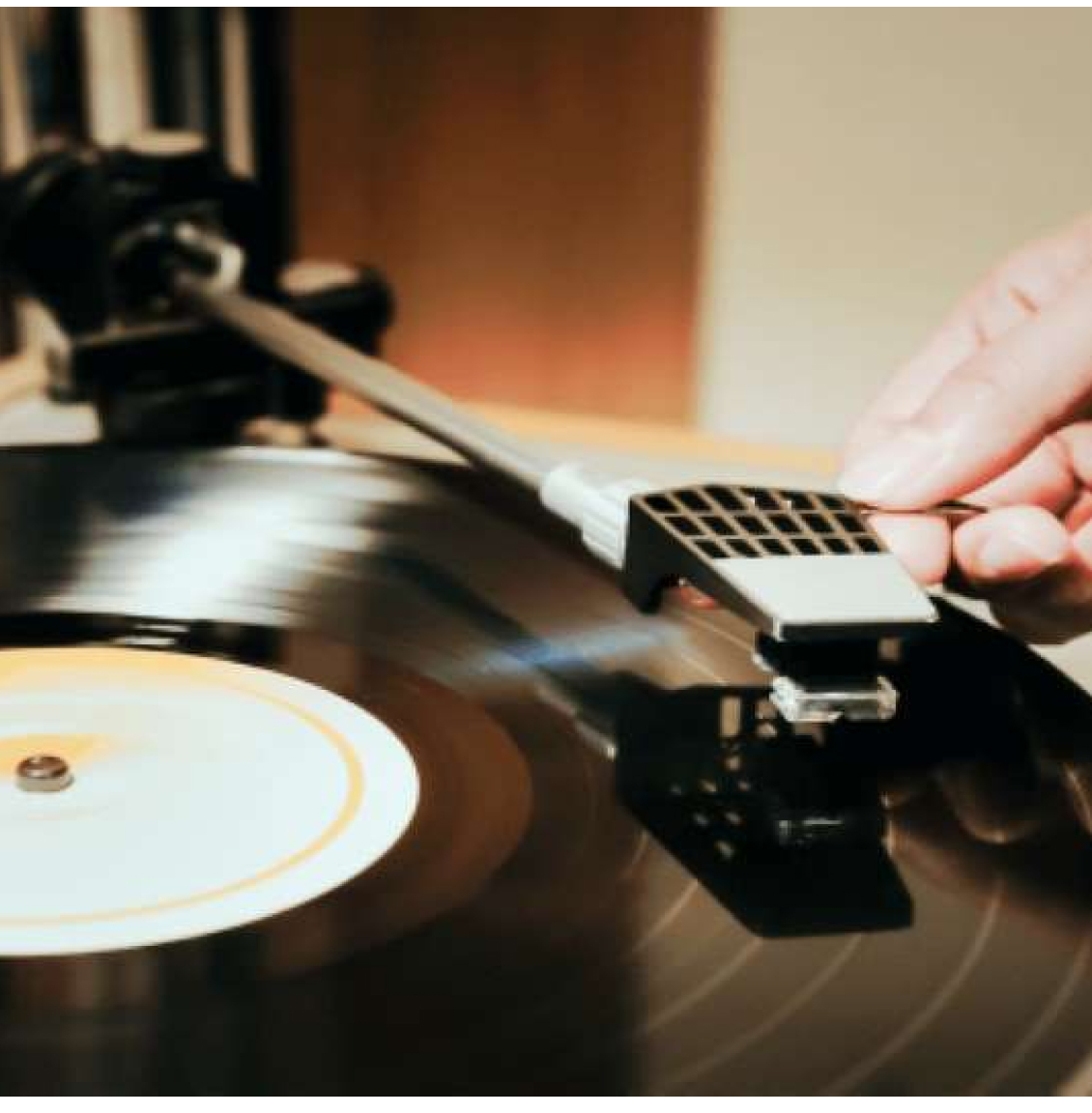 Hand legt Tonarm auf schwarze Schallplatte auf einem Plattenspieler.