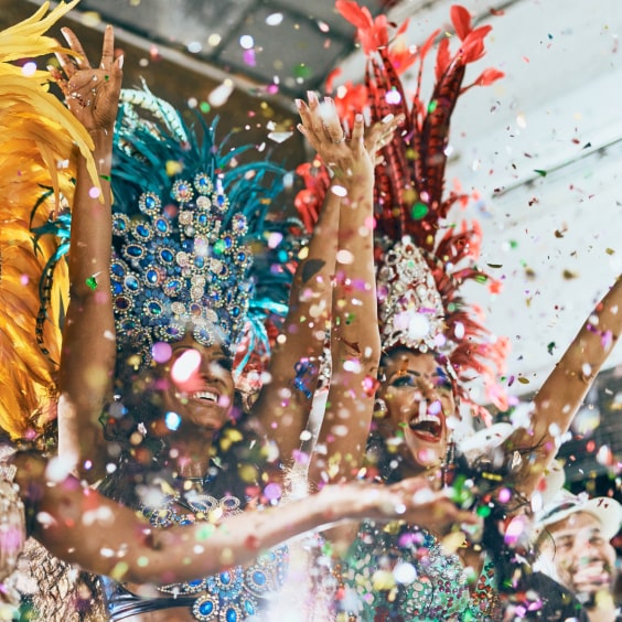 Tänzerinnen in bunten Federkostümen jubeln unter Konfettiregen.