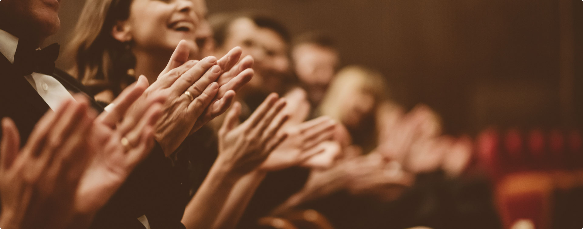 Menschen in Abendkleidung klatschen begeistert in einem Theater oder Konzertsaal.