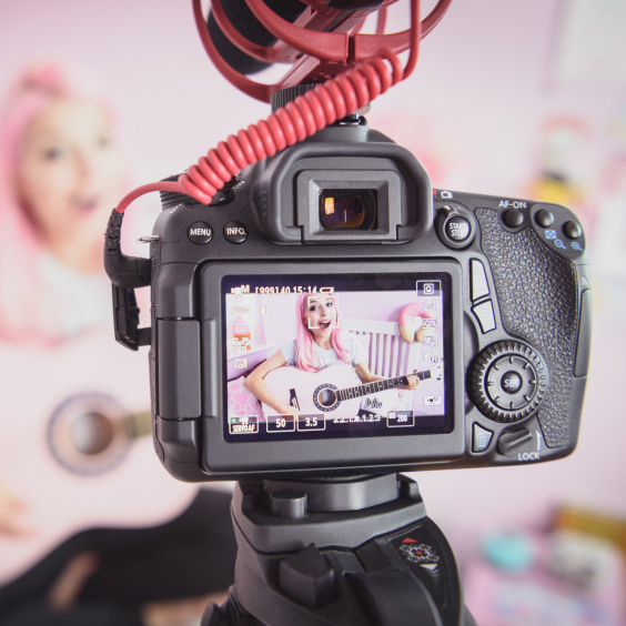 Eine Kamera filmt eine Person mit rosa Haaren, die Gitarre spielt.