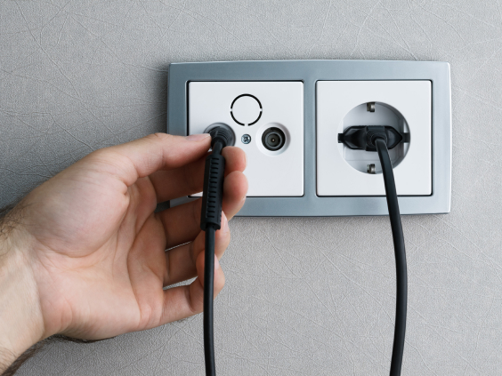 Eine Hand steckt ein Kabel in eine Steckdose neben einer bereits eingesteckten Schuko-Stecker.