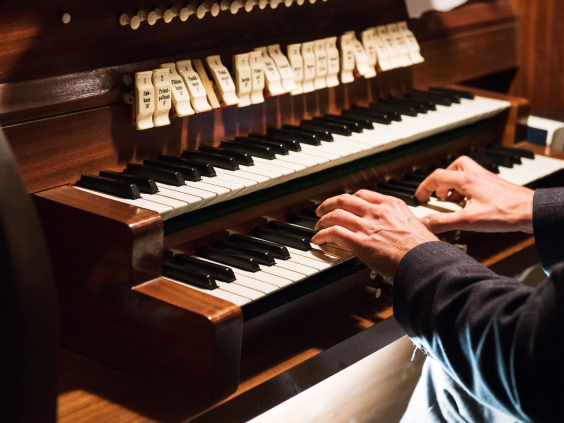 Hände spielen auf einer zweimanualigen Orgel mit Registerzügen.
