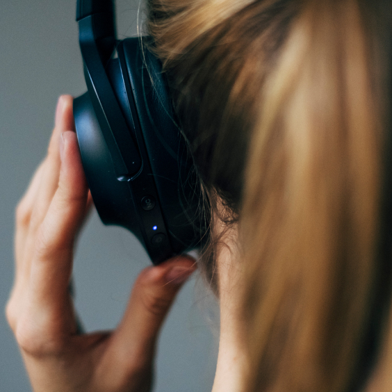 Eine Person mit blonden Haaren trägt schwarze Kopfhörer und hält sie mit der Hand fest.