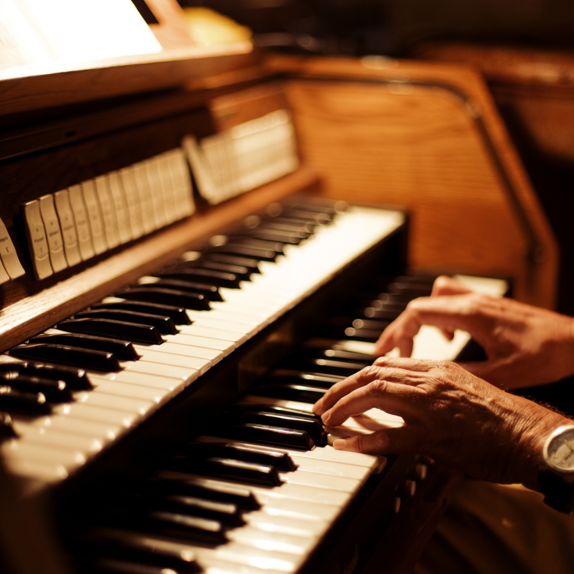 Hände spielen auf einer Orgel mit mehreren Tastenreihen und Holzelementen.