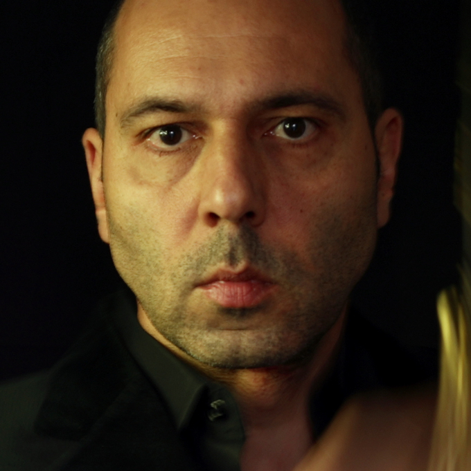 Ein Mann mit ernstem Gesichtsausdruck vor schwarzem Hintergrund.