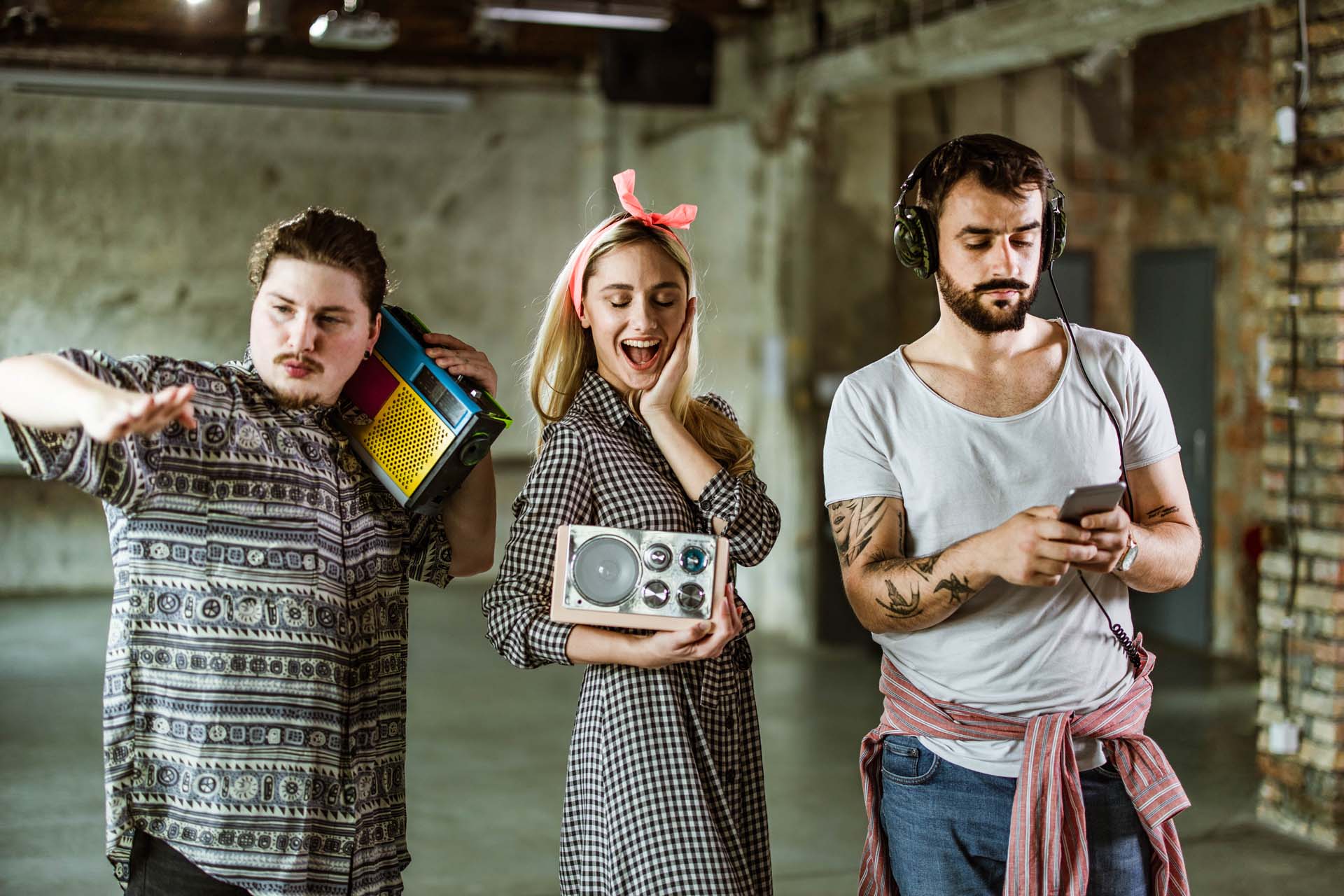 Drei Personen mit Retro-Radios und Kopfhörern in einem industriellen Raum.