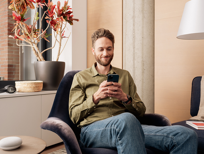 Ein Mann in grünem Hemd sitzt lächelnd auf einem Sessel und schaut auf sein Smartphone.