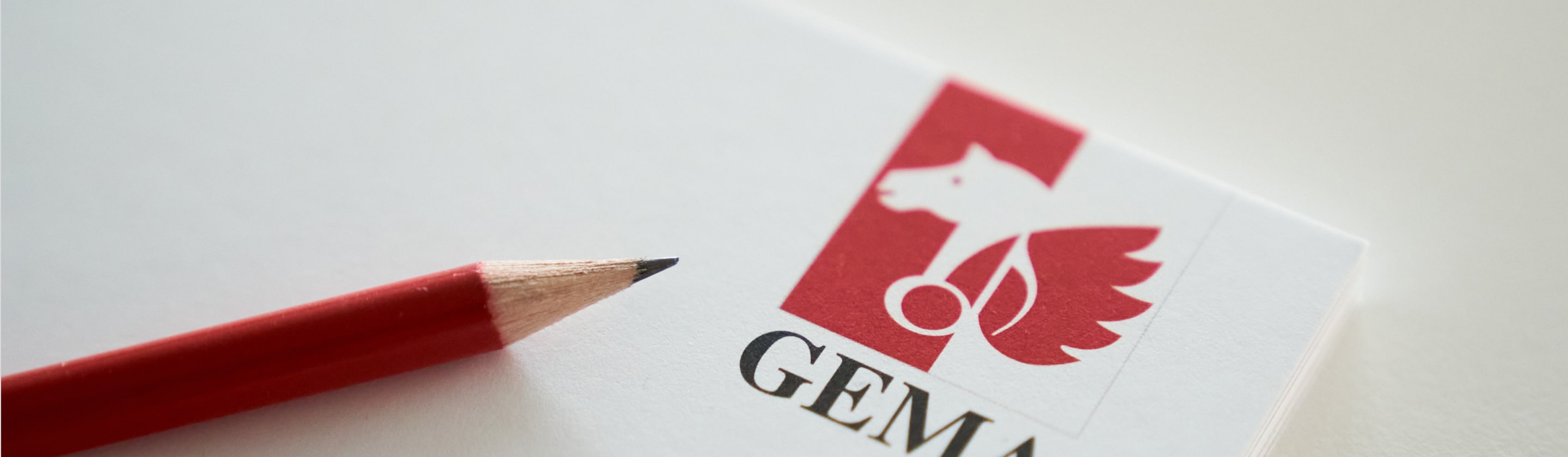 Roter Bleistift auf Papier mit rotem Logo eines geflügelten Pferdes und dem Schriftzug 