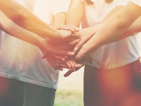 Mehrere Hände übereinander gestapelt, symbolisieren Teamarbeit und Zusammenhalt.