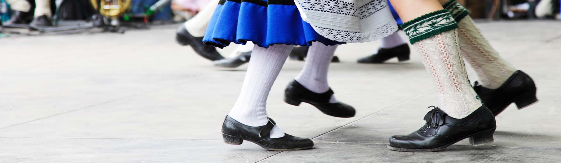 Tänzer in Tracht mit blauen Röcken und weißen Socken tanzen auf einer Bühne.