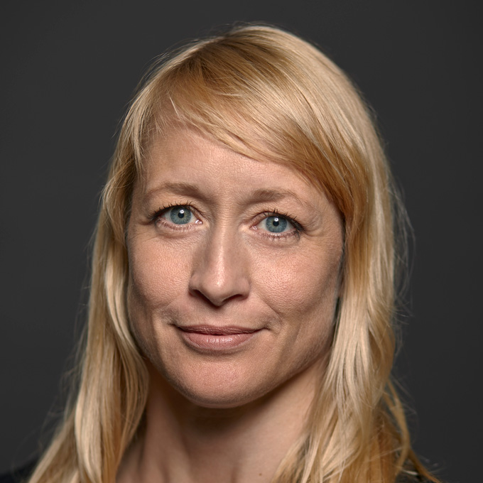 Porträt einer lächelnden Frau mit blonden Haaren vor grauem Hintergrund.