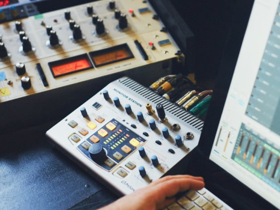 Tonstudio mit Mischpult, Kabeln und Computerbildschirm, Hand auf Tastatur.