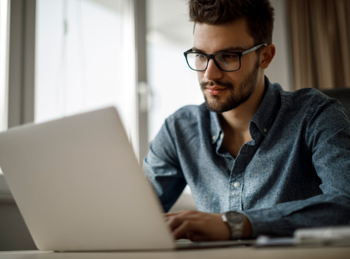 Ein Mann mit Brille arbeitet konzentriert an einem Laptop in einem hellen Raum.