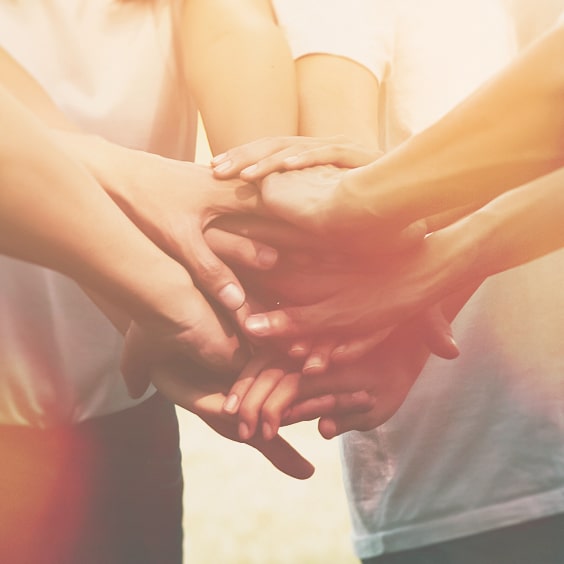 Mehrere Hände übereinander gestapelt, symbolisieren Teamarbeit und Zusammenhalt.